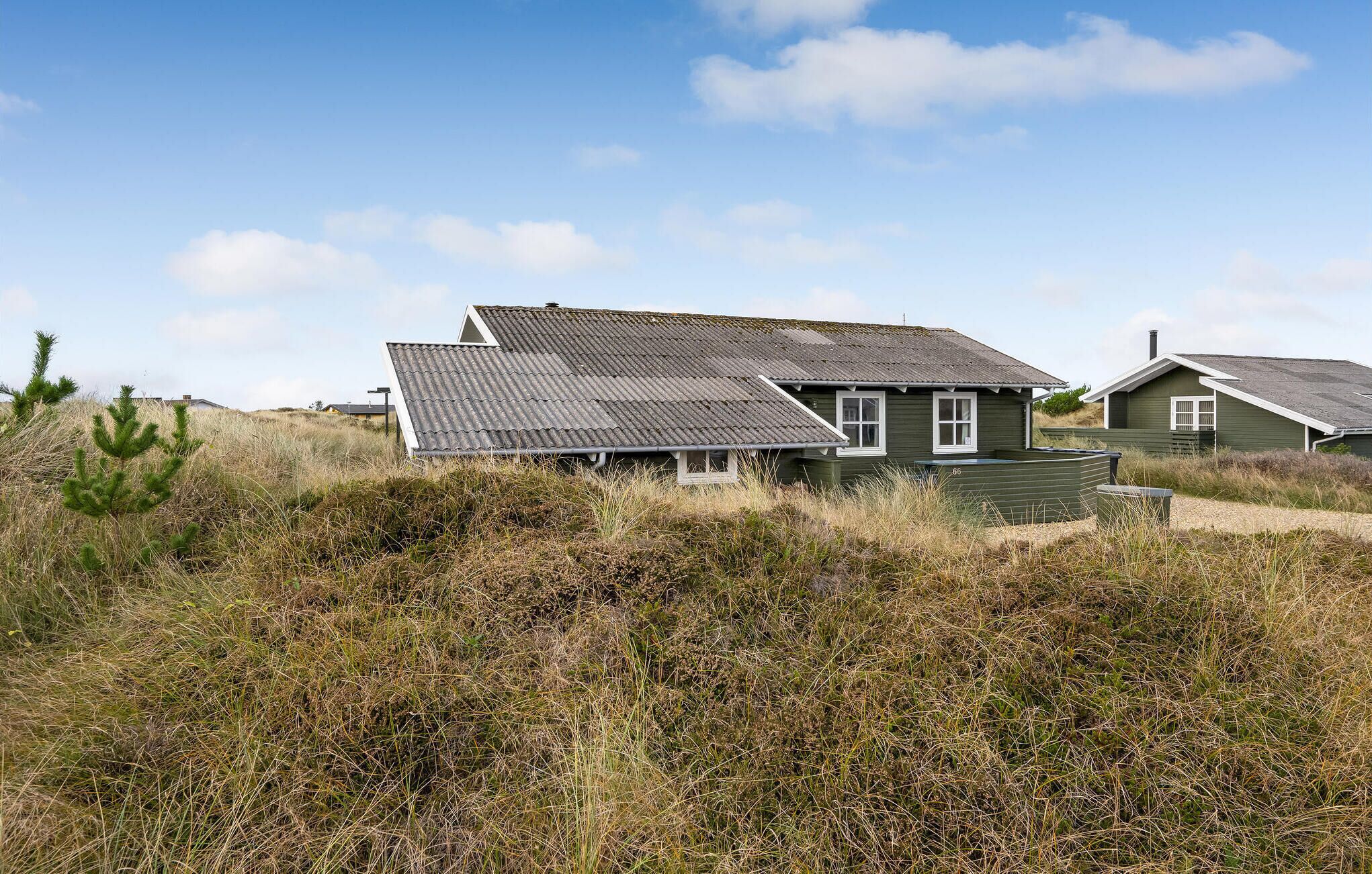 Ein Küstenhaus mit geneigtem Dach, umgeben von hohem Gras und Dünen.
