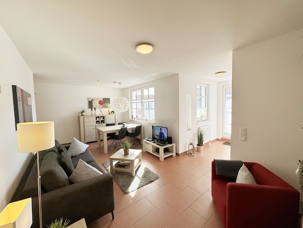 A spacious living area with a sofa, a red armchair, a dining table, and a TV.