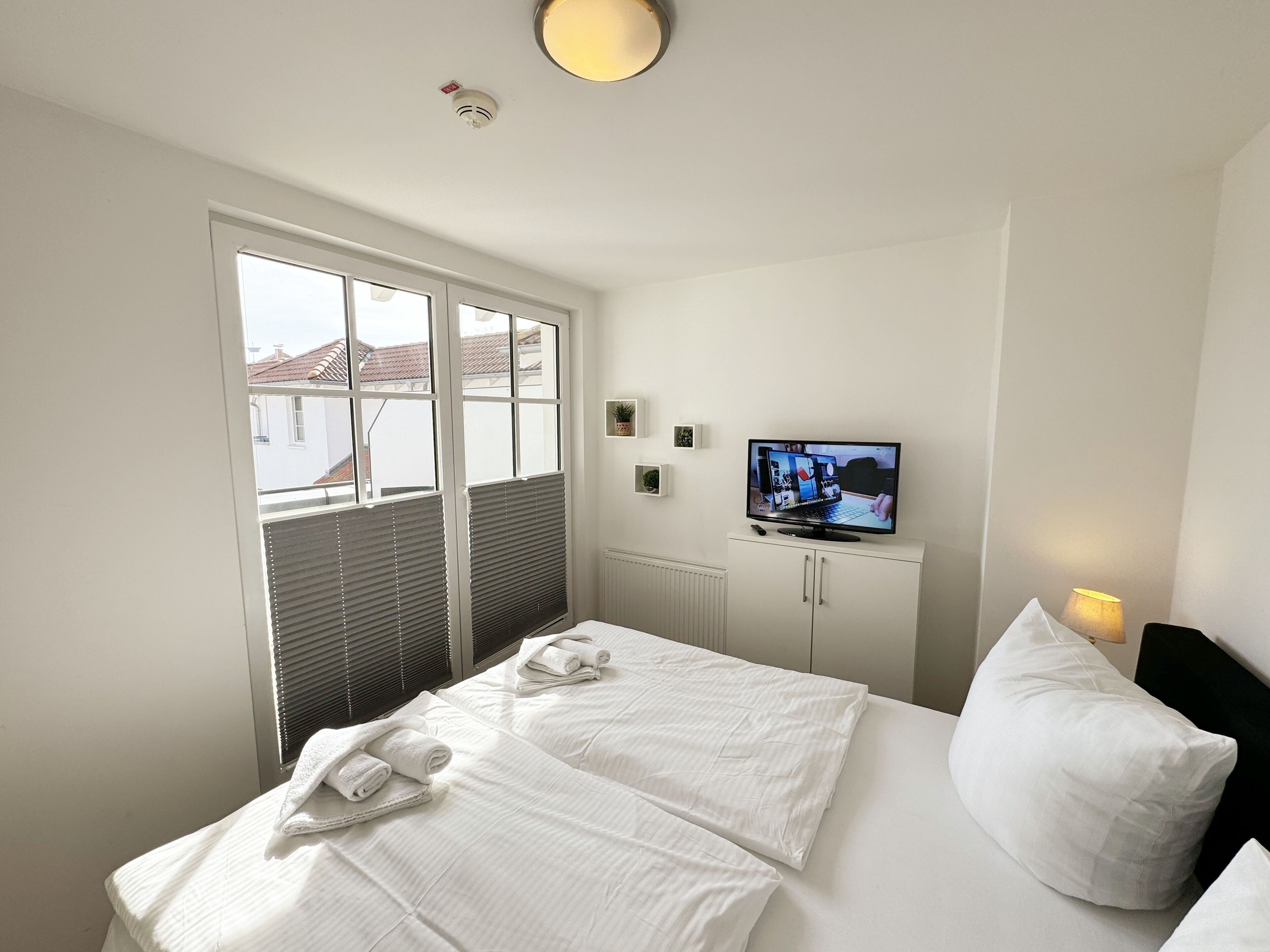 A hotel room with a bed, a television, and a window with blinds.