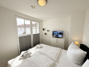 A hotel room with a bed, a television, and a window with blinds.