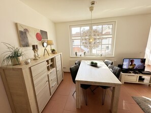 A modern living room with a dining table, chairs, a TV, and a window with a decorative light fixture.