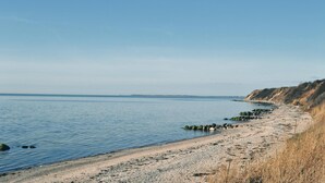 A coastal beach with a pebbly shore, calm water, and a cliff in the background. - 2 bedroom lovely home in Slagelse (Slagelse)