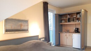 A bedroom with a bed, a painting, a kitchenette with a microwave, and a coffee maker. - (274) 1-room apartment - apartment complex Yachthafenresidenz (Kühlungsborn)