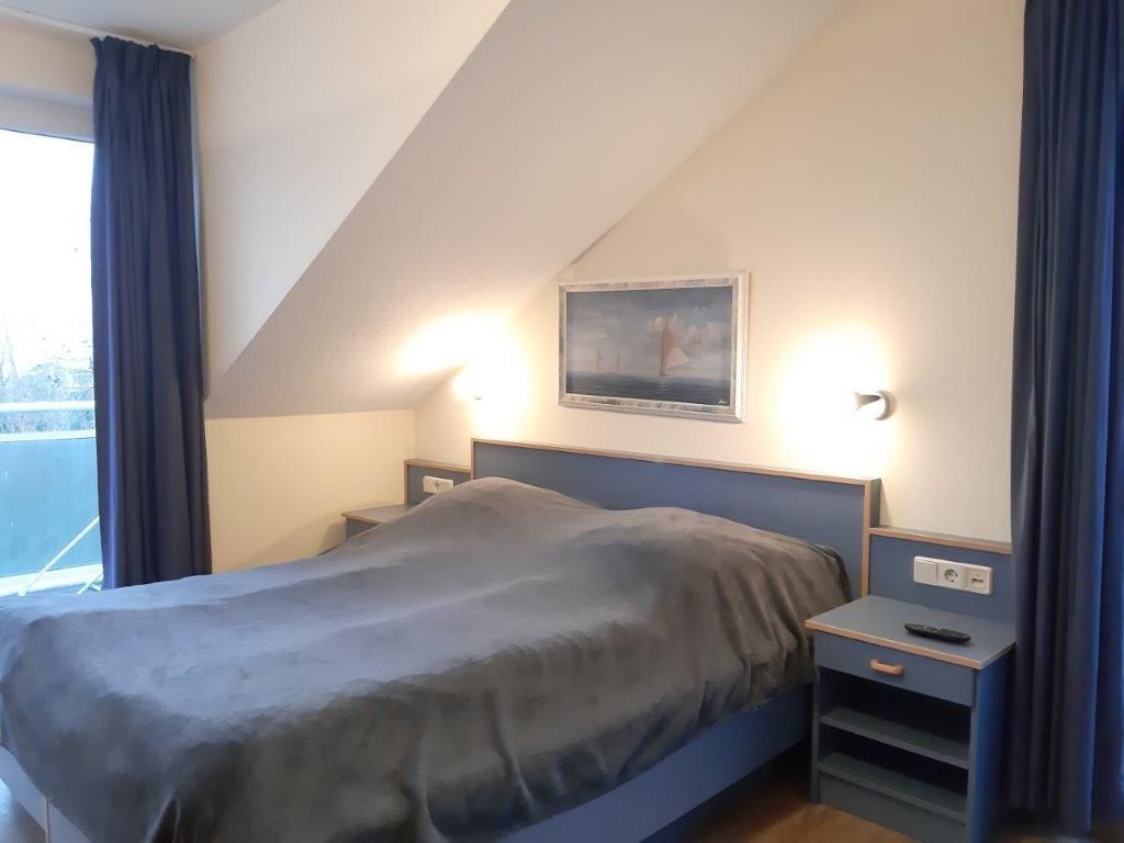 Een slaapkamer met een bed, nachtkastjes, een schilderij en een raam met gordijnen.