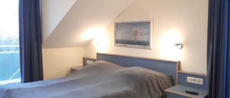 Een slaapkamer met een bed, nachtkastjes, een schilderij en een raam met gordijnen.