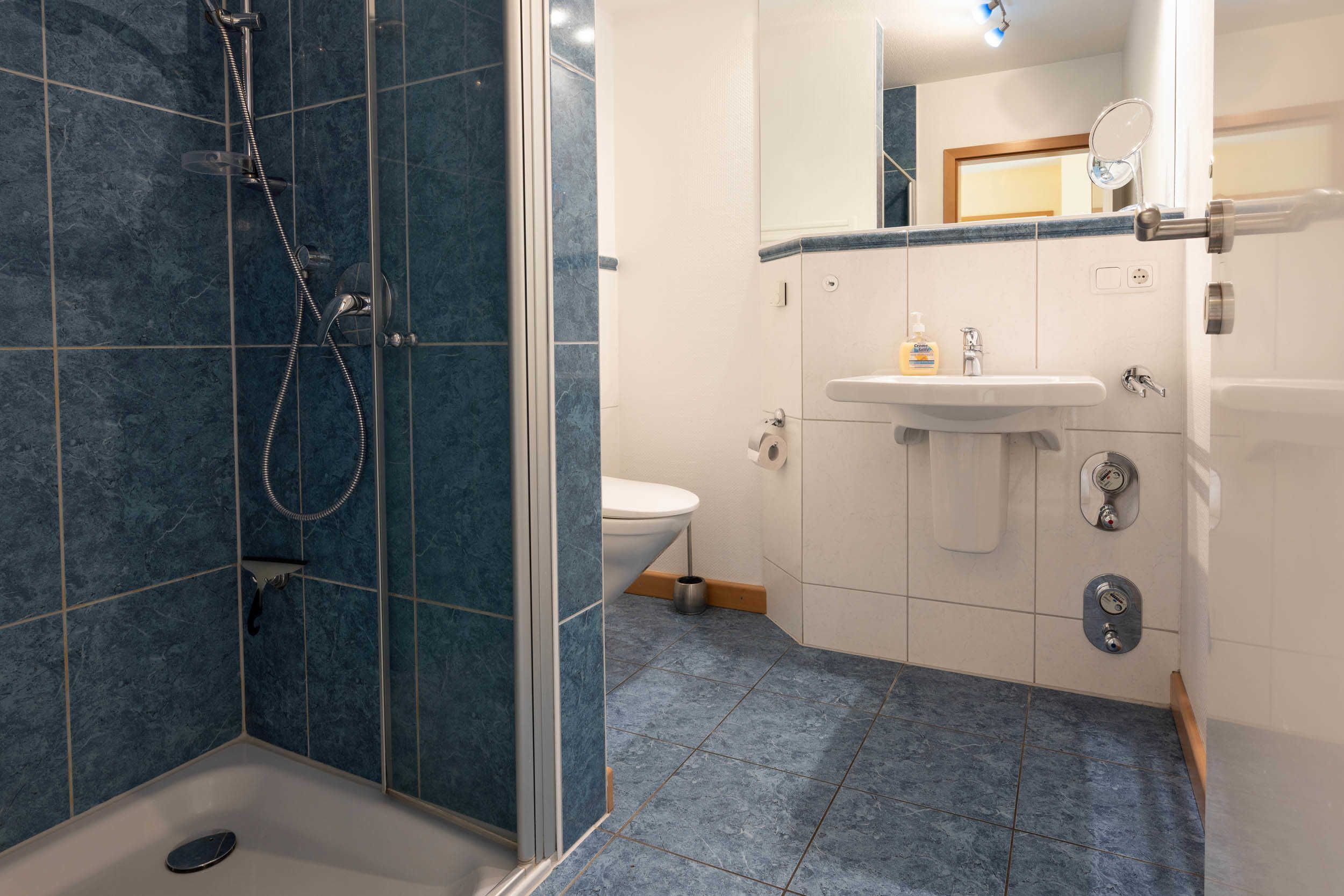 A bathroom with a shower, toilet, sink, and mirror.