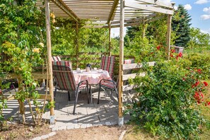 A covered outdoor dining area with a table and chairs, surrounded by lush greenery and flowering plants.