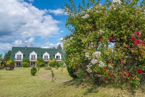 A three-story house with a green roof, surrounded by a well-maintained lawn and flowering bushes.