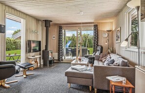 Relax in a warm and inviting space with a sofa, chair, and flat-screen TV, surrounded by a lush garden view.