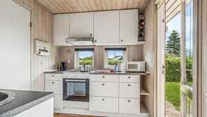 Cozinha compacta com armários brancos, fogão Bosch, micro-ondas e vista para o verde lá fora.