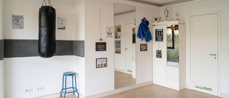 Een kamer met een bokszak, een blauwe kruk, een spiegel en een deur met een spiegel.