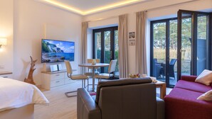 Une chambre d’hôtel comprenant un lit, une télévision, une table à manger avec des chaises, un canapé et un balcon donnant sur la forêt.