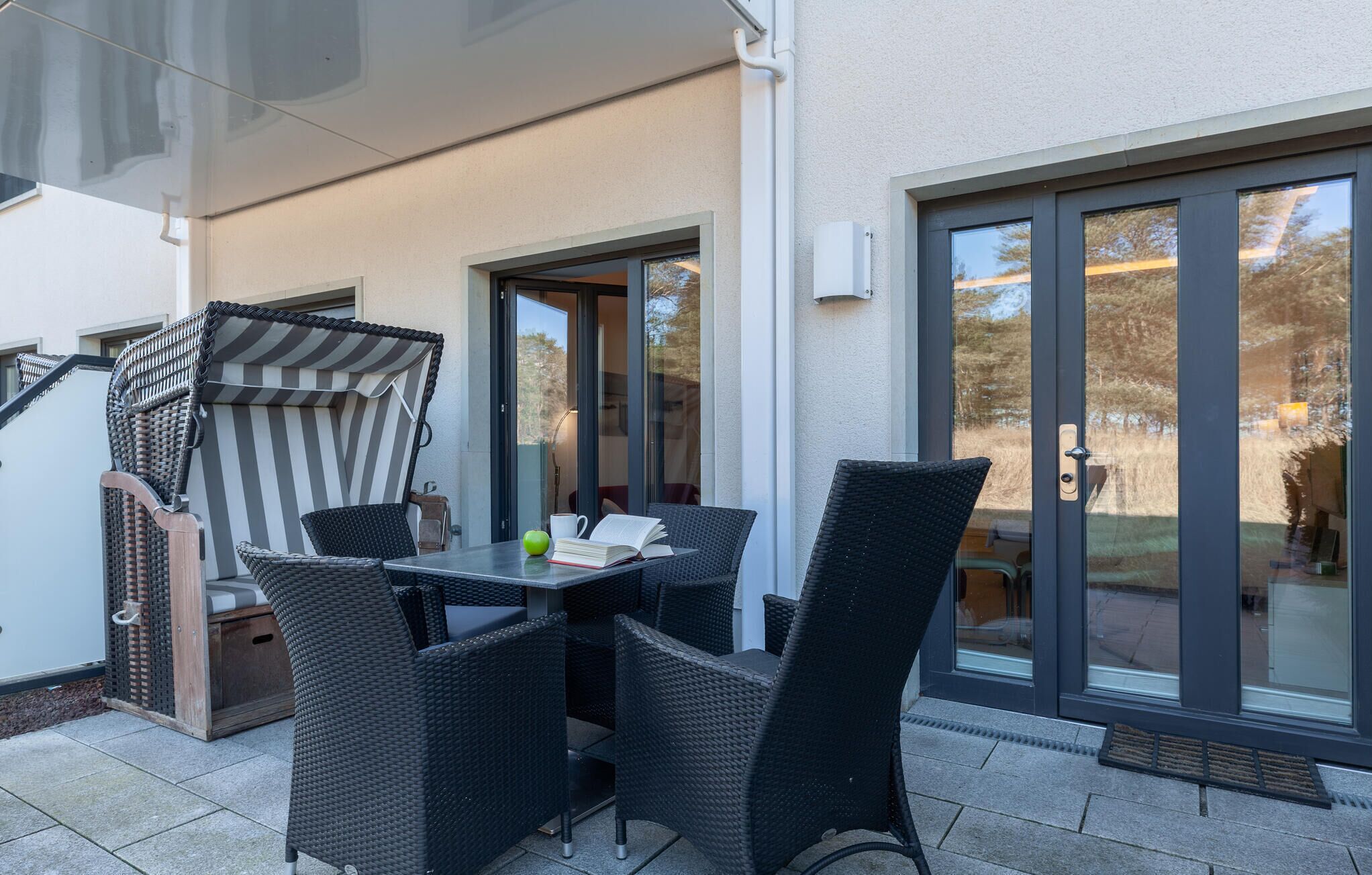Un patio con mobiliario exterior, una mesa con libros y una manzana, y una puerta corrediza de vidrio.