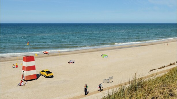 Une plage avec une tour de surveillance pour les sauveteurs, un véhicule jaune et des personnes qui se promènent le long du rivage.