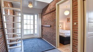 Une pièce avec un mur en briques, un lit, une échelle et une porte donnant sur une autre pièce.