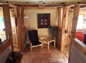 A cozy room with wooden walls and a tiled floor, featuring a chair, a small table, a lamp, and a decorative wall piece.