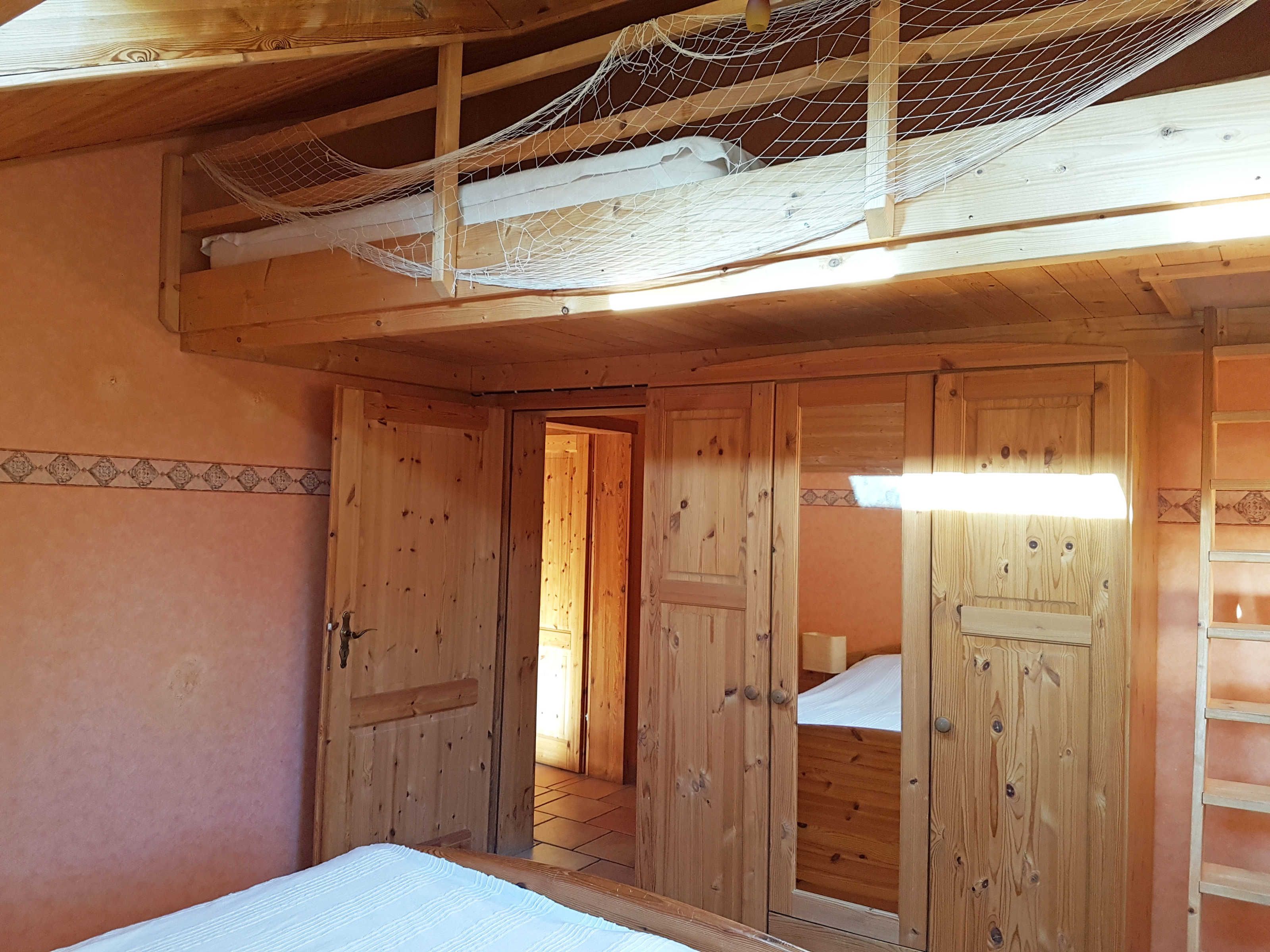 A wooden room with a bed, a door leading to another room, and a ladder against the wall.