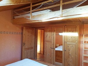A wooden room with a bed, a door leading to another room, and a ladder against the wall.