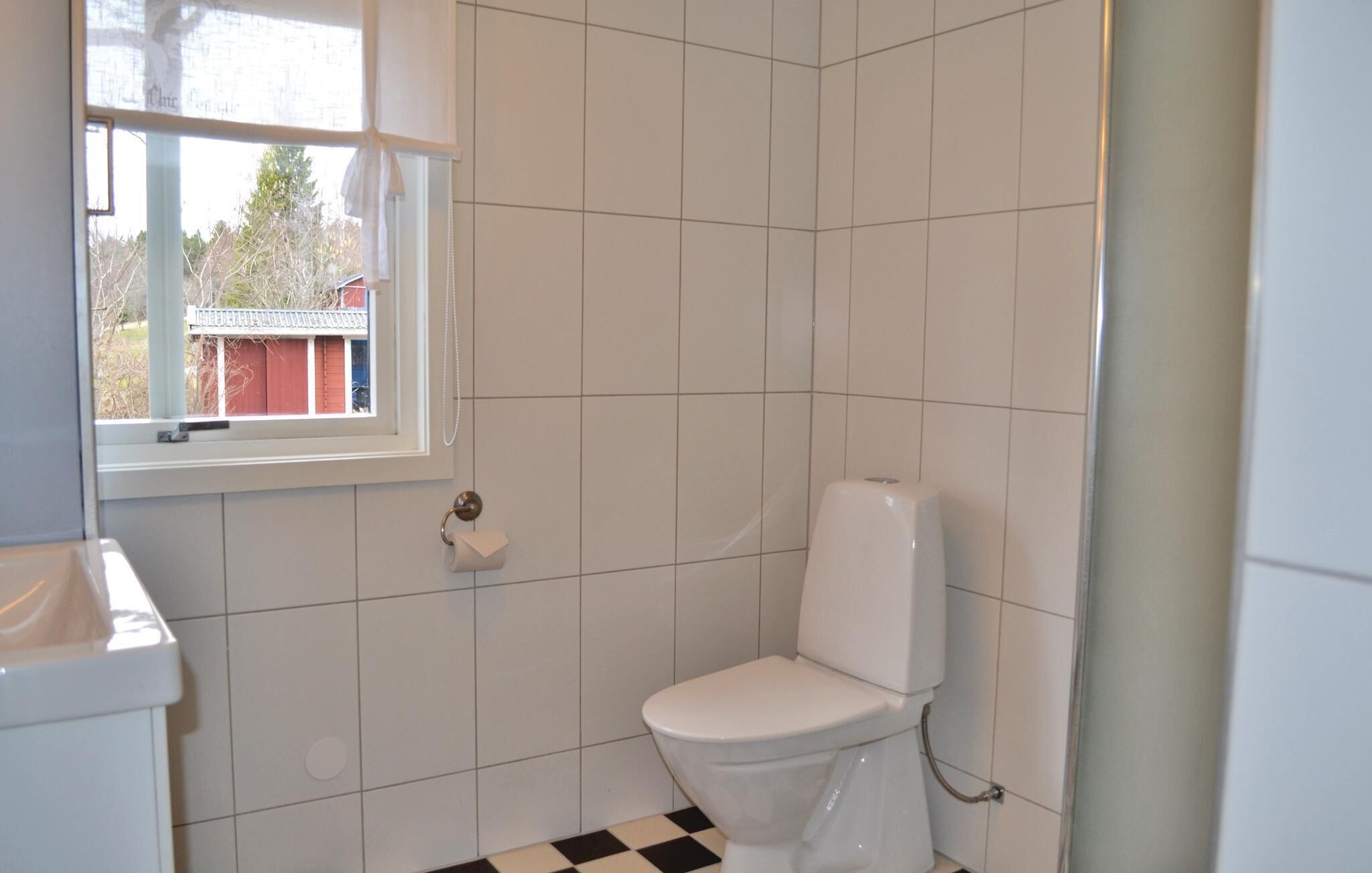Un baño pequeño y limpio con azulejos blancos, un inodoro, una ventana y vistas al exterior.