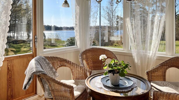A cozy room with wicker furniture, a glass table with a vase, and a view of a lake through large windows. - Amazing home in Köpmannebro with WiFi (Köpmannebro)
