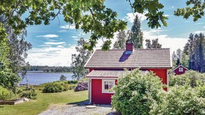 A red cabin with a tiled roof, surrounded by greenery and a lake. - Amazing home in Köpmannebro with WiFi (Köpmannebro)