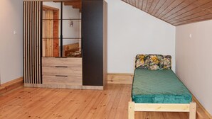 A small, cozy room with a wooden floor, a single bed with a floral pillow, and a sliding door leading to another room. - Cozy home in Biskupice with WiFi (Biskupice)