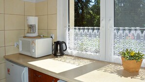 A kitchen with a microwave, coffee maker, and a window with a white lace curtain. - Cozy home in Biskupice with WiFi (Biskupice)