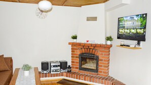 A living room with a brick fireplace, a television mounted on the wall, and a wooden ceiling. - Cozy home in Biskupice with WiFi (Biskupice)