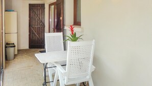 A small, enclosed outdoor dining area with a white table and two white chairs, a potted plant, and a wooden door.