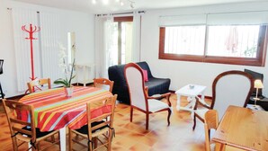 A dining area with a striped tablecloth, wooden chairs, a black sofa, and a window with blinds.