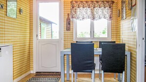 Een klein eetgedeelte met een tafel, stoelen, een raam met bloemenstoffering en een deur.