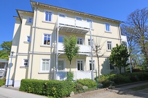A multi-story building with a balcony on the second floor, surrounded by greenery and a fence. - P: Villa Strandmuschel Whg. 05 - approx. 100m from the beach - Villa Strandmuschel (Sellin)