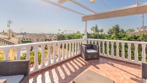 Een balkon met een witte balustrade, een rieten bank en een kleine tafel.