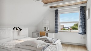 Une chambre à coucher avec un lit, un bureau, une chaise, un miroir et une fenêtre avec des rideaux.