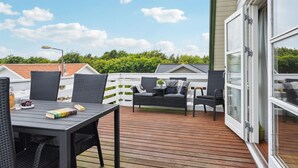Une terrasse en bois, aménagée avec du mobilier d’extérieur, notamment une table et des chaises, et une porte vitrée donnant sur un espace abrité.