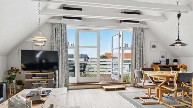 Un salon moderne doté d’un téléviseur à écran plat, d’un coin repas avec des meubles en bois et d’un balcon offrant une vue sur les bâtiments.