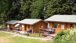 A row of wooden cabins with porches, each featuring a table and chairs. - Double Room Disability Access - Ferienpark Plauer See (Alt Schwerin)