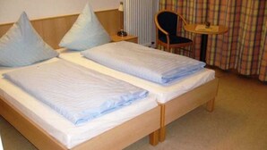 A double bed with a wooden frame, two pillows, a bedside table with a lamp, and a chair with a table. - Double Room Disability Access - Ferienpark Plauer See (Alt Schwerin)
