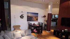 Ein modernes Wohnzimmer mit einem grauen Ecksofa, einem Esstisch mit Stühlen, einem kleinen runden Couchtisch und einem an der Wand befestigten Flachbildfernseher.