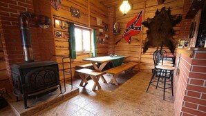 A rustic cabin interior with a wood-burning stove, a table with benches, and a flag on the wall. - Holiday home with outdoor pool and Western-style restaurant (Vlcice)