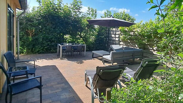 Eine Terrassenanlage im Freien mit Tisch, Stühlen und einer Sitzecke, sowie einem Sonnenschirm.