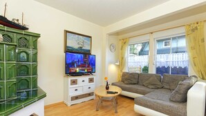 Un salon avec un meuble vert, une télévision, un canapé et une fenêtre avec des rideaux.