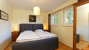Une chambre à coucher avec un grand lit, deux tables de chevet avec des lampes, une fenêtre avec des rideaux et une porte en bois.