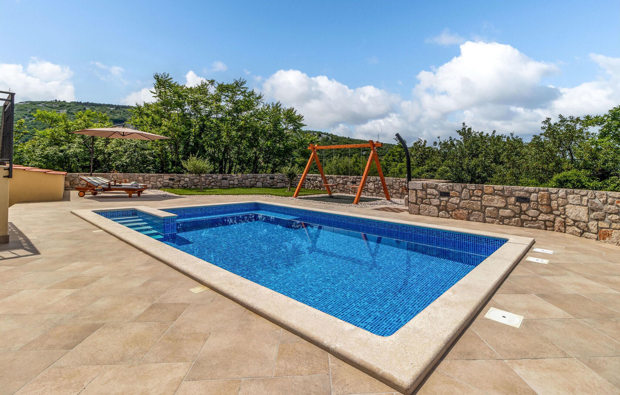 A rectangular swimming pool with a stone wall and a swing set.