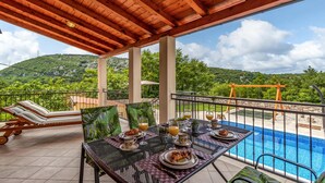 A covered outdoor dining area with a pool view, featuring tables set for breakfast with croissants and orange juice, and lounge chairs. - Gorgeous home in Barci (Barci)