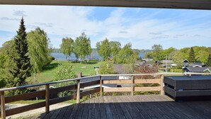 Una terraza de madera con vista a un lago, rodeada de árboles y casas.