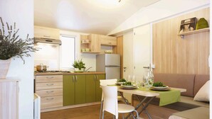 A compact kitchen with a dining area, featuring a foldable table, a white chair, and a sofa. - Victoria Mobilehome Bi Village (Fazana)