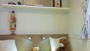 A hotel room with two single beds, a small table with a lamp, a shelf with a toy car and a framed picture, and a teddy bear on one bed. - Victoria Mobilehome Bi Village (Fazana)