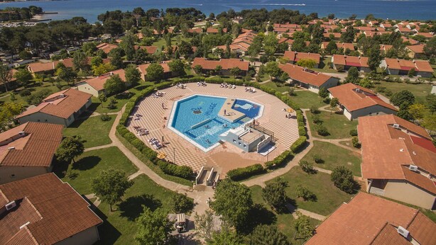 An aerial view of a residential area with a central swimming pool surrounded by houses with red-tiled roofs. - Victoria Mobilehome Bi Village (Fazana)