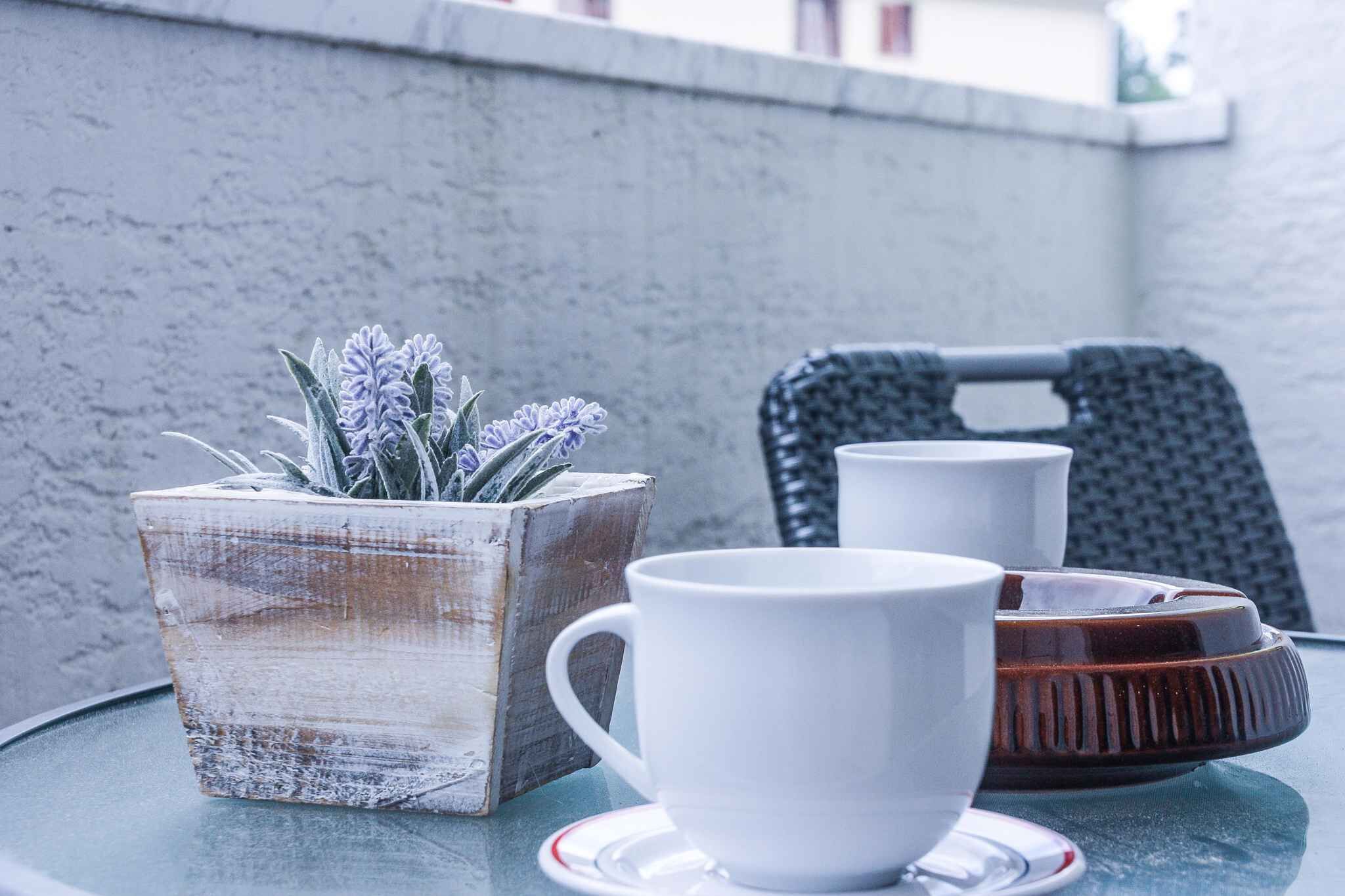 Ein Tisch mit einer weißen Tasse, einem braunen Tablett und einem Blumentopf mit violetten Blüten.